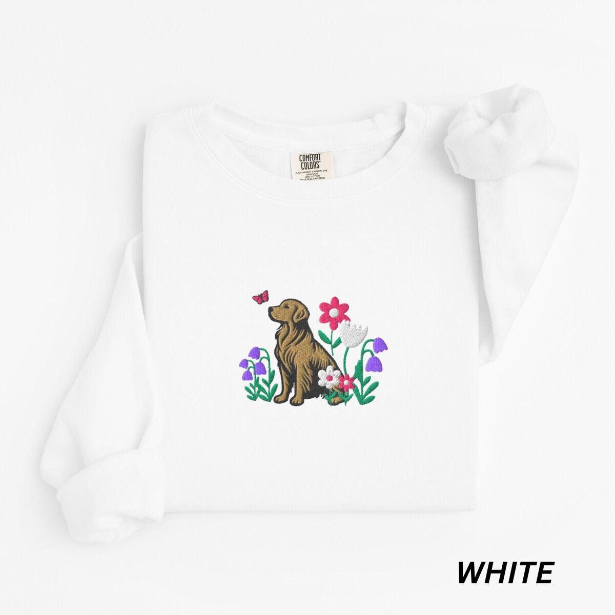 Golden Retriever Flower Sweatshirt – White White crewneck sweatshirt laid flat, embroidered with a sitting golden retriever among spring flowers and a pink butterfly