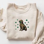 Sand crewneck sweatshirt laid flat, embroidered with a sitting golden retriever holding a four leaf clover in its mouth, ringed by green shamrocks