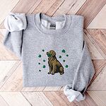 Sport Grey crewneck sweatshirt laid flat on a wood floor, embroidered with a sitting golden retriever holding a four leaf clover in its mouth, ringed by green shamrocks
