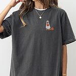 Woman in an oversized Pepper T-shirt embroidered with a golden retriever in a white ghost sheet carrying a jack-o'-lantern bucket beside a small pumpkin on the left chest