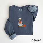 Denim crewneck sweatshirt folded flat with a rolled cuff, embroidered with a golden retriever in a white ghost sheet carrying a jack-o'-lantern trick-or-treat bucket beside a small pumpkin