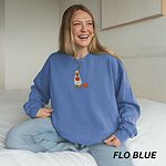 Woman sitting on a bed in a Flo Blue crewneck sweatshirt embroidered with a golden retriever in a white ghost sheet carrying a jack-o'-lantern trick-or-treat bucket beside a small pumpkin