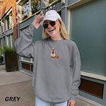Woman in a white cap and sunglasses wearing a Grey crewneck sweatshirt embroidered with a golden retriever in a white ghost sheet carrying a jack-o'-lantern trick-or-treat bucket beside a small pumpkin