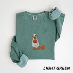 Light Green crewneck sweatshirt folded flat with a rolled cuff, embroidered with a golden retriever in a white ghost sheet carrying a jack-o'-lantern trick-or-treat bucket beside a small pumpkin
