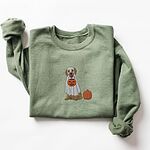 Military Green crewneck sweatshirt laid flat with one sleeve raised, embroidered with a golden retriever in a white ghost sheet carrying a jack-o'-lantern trick-or-treat bucket beside a small pumpkin