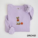 Orchid crewneck sweatshirt folded flat with a rolled cuff, embroidered with a golden retriever in a white ghost sheet carrying a jack-o'-lantern trick-or-treat bucket beside a small pumpkin