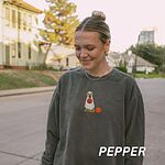 Woman walking down a street in a Pepper crewneck sweatshirt embroidered with a golden retriever in a white ghost sheet carrying a jack-o'-lantern trick-or-treat bucket beside a small pumpkin