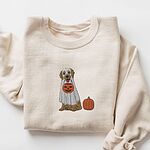 Sand crewneck sweatshirt laid flat with a rolled sleeve, embroidered with a golden retriever in a white ghost sheet carrying a jack-o'-lantern trick-or-treat bucket beside a small pumpkin