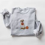 Sport Grey crewneck sweatshirt laid flat with folded sleeves, embroidered with a golden retriever in a white ghost sheet carrying a jack-o'-lantern trick-or-treat bucket beside a small pumpkin