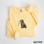 Butter crewneck sweatshirt laid flat, embroidered with a golden retriever carrying a strand of red, green, yellow and blue bulbs