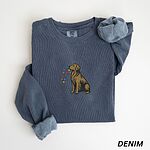 Denim crewneck sweatshirt laid flat, embroidered with a golden retriever holding Christmas lights in the middle of the chest