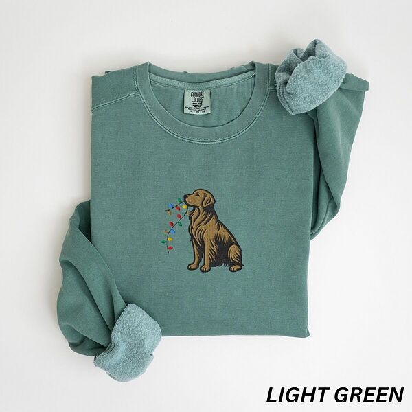 Golden retriever holding Christmas lights sweatshirt in Light Green laid flat with rolled cuffs, embroidered with a sitting golden carrying a strand of colored bulbs