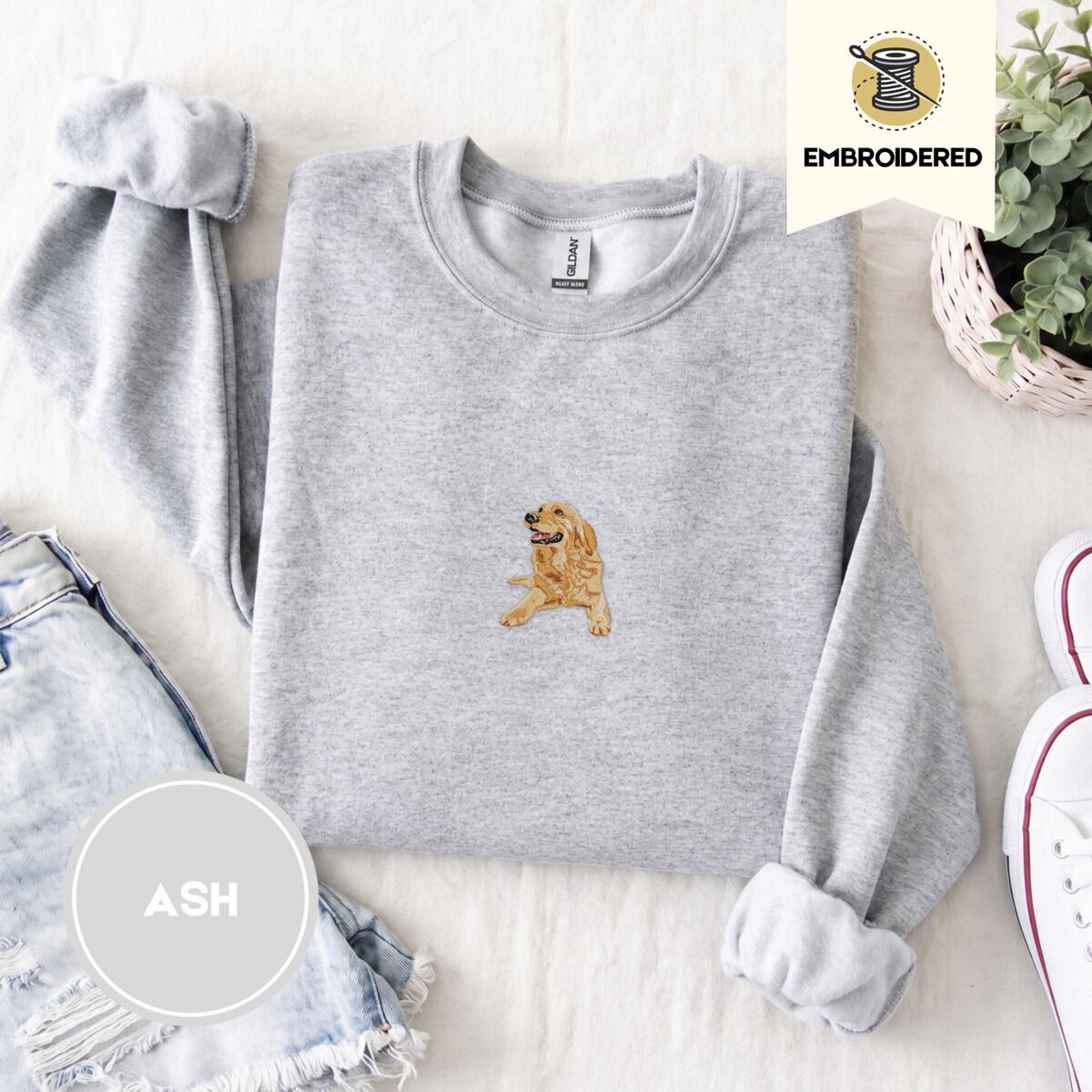 Golden Retriever Mom Sweatshirt – Ash Ash crewneck sweatshirt folded with denim shorts, white sneakers and a potted plant, embroidered with a happy golden retriever lying down with its head up and tongue out