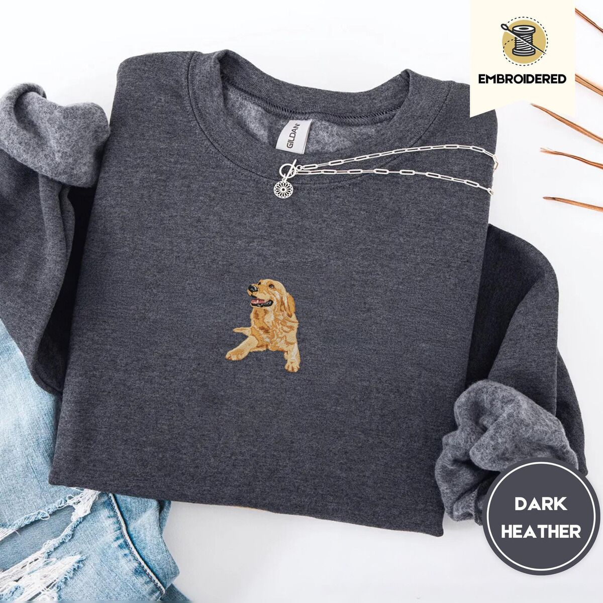Golden Retriever Mom Sweatshirt – Dark Heather Dark Heather crewneck sweatshirt folded with ripped jeans and a silver chain necklace, embroidered with a happy golden retriever lying down with its head up and tongue out