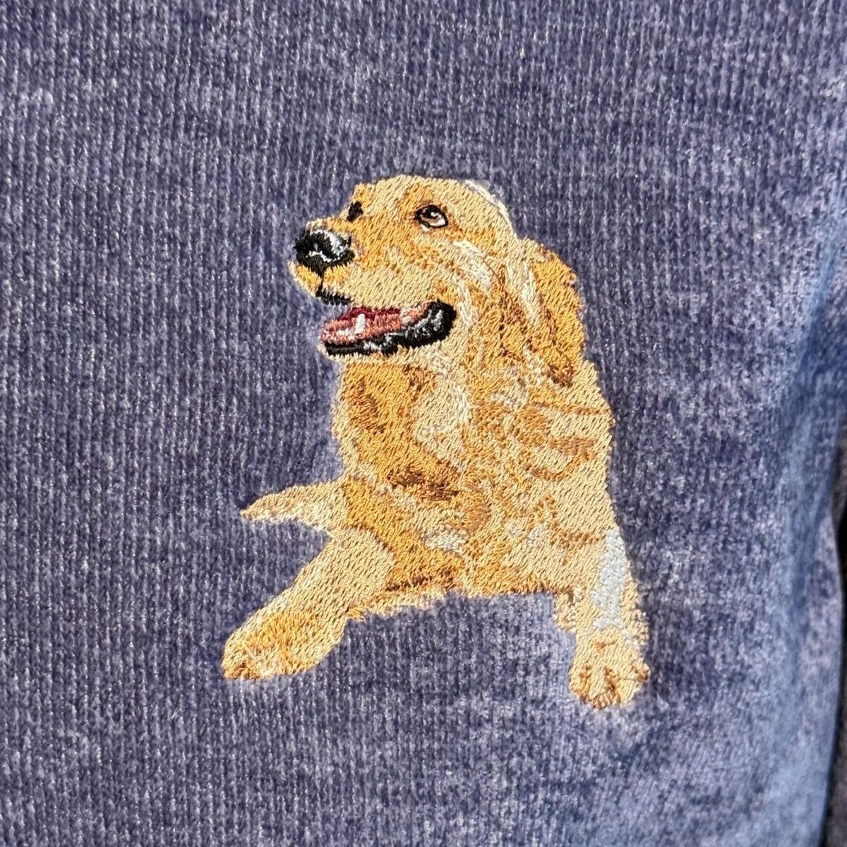 Golden Retriever Embroidery Close-Up Close-up of a real stitched golden retriever lying down with its head up and tongue out, in layers of gold, honey and cream thread on a blue sweatshirt