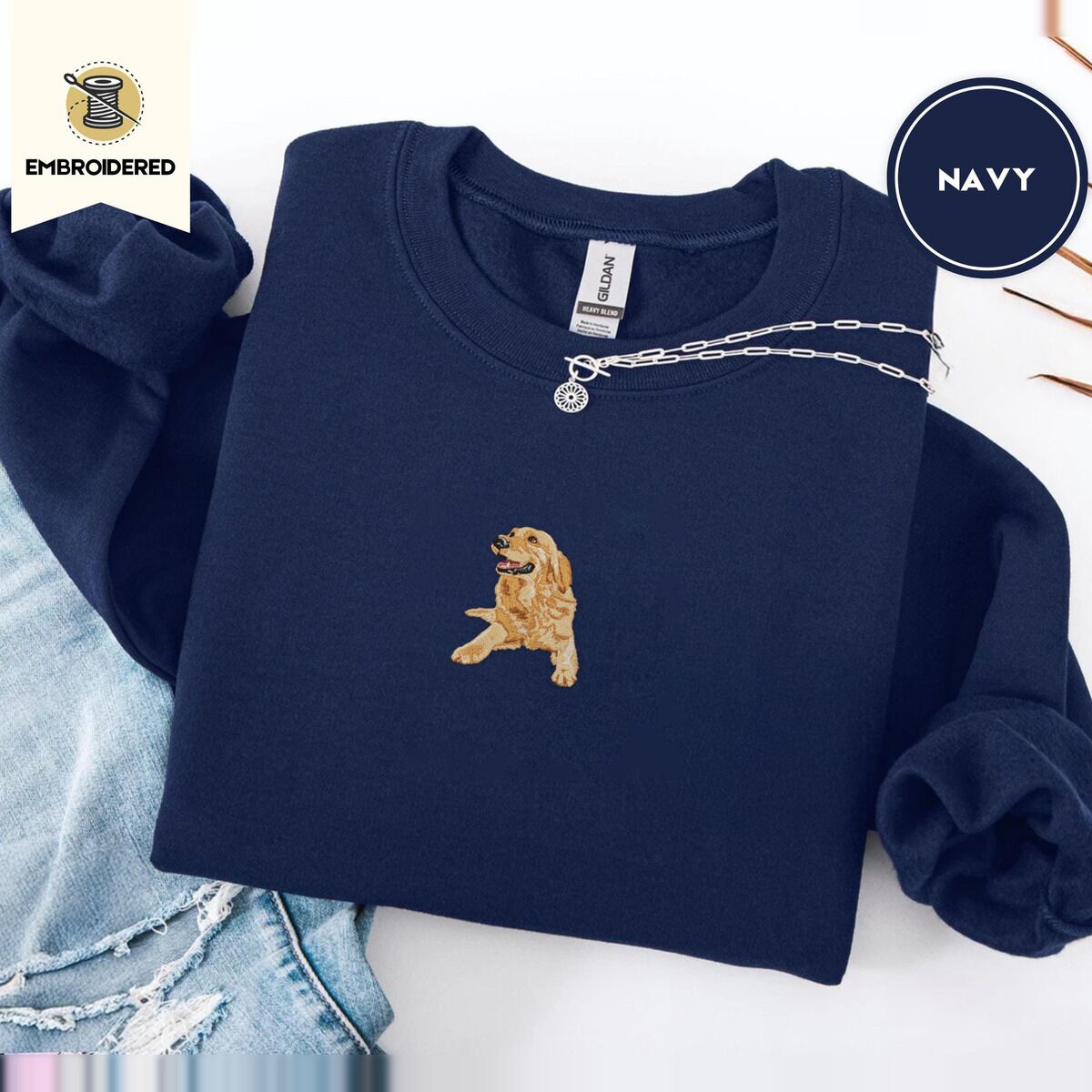Golden Retriever Mom Sweatshirt – Navy Navy crewneck sweatshirt folded with ripped jeans and a silver chain necklace, embroidered with a happy golden retriever lying down with its head up and tongue out