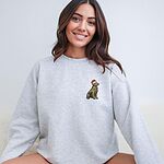 Smiling woman sitting in an Ash crewneck sweatshirt embroidered with a small golden retriever in a red Santa hat