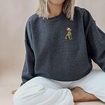 Woman sitting cross-legged in a Dark Heather crewneck sweatshirt embroidered with a golden retriever in a red Santa hat