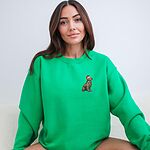 Woman sitting in an Irish Green crewneck sweatshirt embroidered with a small golden retriever in a red Santa hat