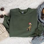 Military Green crewneck sweatshirt on a faux fur throw with pinecones and a knit beanie, embroidered with a golden retriever in a Santa hat on the left chest