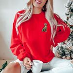 Woman by a frosted Christmas tree in a Red crewneck sweatshirt embroidered with a small golden retriever in a Santa hat