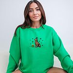 Smiling woman in a Irish Green crewneck sweatshirt embroidered with a sitting golden retriever in a green leprechaun hat with a pot of gold and green shamrocks