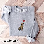 Sport Grey crewneck sweatshirt laid flat on a wood floor, embroidered with a sitting golden retriever holding the string of a red heart balloon in its mouth