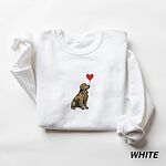 White crewneck sweatshirt laid flat, embroidered with a sitting golden retriever holding the string of a red heart balloon in its mouth