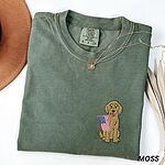 Moss T-shirt folded beside a hat, a curly goldendoodle with a stars-and-stripes flag on the left chest