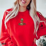 Woman by a frosted Christmas tree in a Red crewneck sweatshirt embroidered with a goldendoodle between two presents