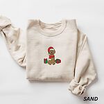 Sand crewneck sweatshirt laid flat, embroidered with a golden doodle in a Santa hat and scarf sitting between wrapped gifts