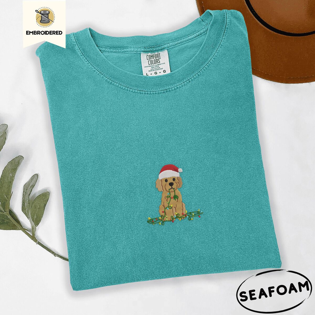 Goldendoodle Christmas Shirt – Seafoam Seafoam Comfort Colors T-shirt embroidered with a curly apricot goldendoodle puppy in a Santa hat chewing on a tangled string of Christmas lights