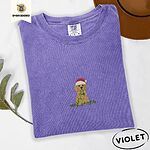 Violet Comfort Colors T-shirt embroidered with a curly apricot goldendoodle puppy in a Santa hat chewing on a tangled string of Christmas lights