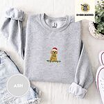 Ash crewneck sweatshirt folded with denim shorts, white sneakers and a potted plant, embroidered with a goldendoodle puppy in a Santa hat chewing on a tangled string of Christmas lights
