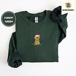 Forest Green crewneck sweatshirt folded on a white background, embroidered with a goldendoodle puppy in a Santa hat chewing on a tangled string of Christmas lights