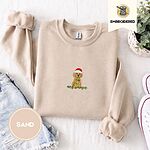 Sand crewneck sweatshirt folded with denim shorts, white sneakers and a potted plant, embroidered with a goldendoodle puppy in a Santa hat chewing on a tangled string of Christmas lights