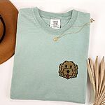Bay T-shirt laid flat with a hat and a necklace, embroidered with a shaggy golden doodle face on the left chest