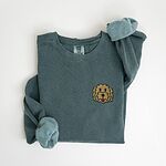 Blue Spruce crewneck sweatshirt laid flat with a rolled cuff, embroidered with a small shaggy golden doodle face on the left chest