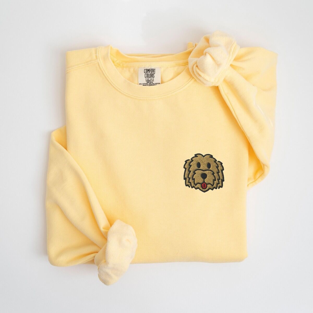Goldendoodle Face Sweatshirt – Butter Butter crewneck sweatshirt laid flat with a knotted sleeve, embroidered with a small shaggy golden doodle face on the left chest