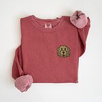 Crimson crewneck sweatshirt laid flat with a knotted sleeve, embroidered with a small shaggy golden doodle face on the left chest