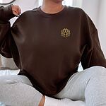 Woman sitting in an oversized Dark Chocolate crewneck sweatshirt embroidered with a small golden doodle face on the left chest