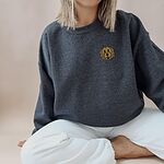 Woman sitting in a Dark Heather crewneck sweatshirt embroidered with a small golden doodle face on the left chest