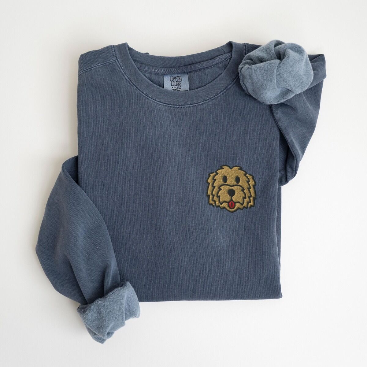Goldendoodle Face Sweatshirt – Denim Denim crewneck sweatshirt laid flat with a rolled cuff, embroidered with a small shaggy golden doodle face on the left chest