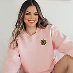 Smiling woman in a Light Pink crewneck sweatshirt embroidered with a small golden doodle face on the left chest