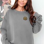 Smiling woman in a Grey crewneck sweatshirt embroidered with a small golden doodle face on the left chest