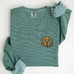 Light Green crewneck sweatshirt laid flat with a rolled cuff, embroidered with a small shaggy golden doodle face on the left chest