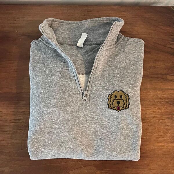 Folded Sport Grey quarter zip pullover on a wooden table, embroidered with a shaggy golden doodle face on the left chest