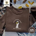 Dark Chocolate crewneck sweatshirt on a plaid flannel shirt with yellow autumn leaves and denim shorts, embroidered with a cool white goose in black sunglasses with arched white lettering embroidered on the chest