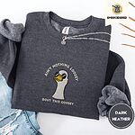 Dark Heather crewneck sweatshirt folded with ripped jeans and a silver chain necklace, embroidered with a cool white goose in black sunglasses with arched white lettering embroidered on the chest