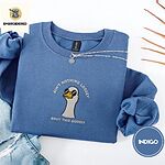 Indigo Blue crewneck sweatshirt folded with light jeans and dried twigs, embroidered with a cool white goose in black sunglasses with arched white lettering embroidered on the chest